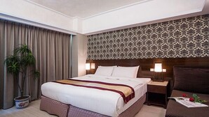 Een hotelkamer met een groot bed, een nachtkastje, een stoel en een potplant.