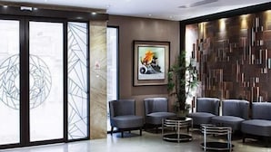 Een moderne lobby met een zithoek, een groot raam met geometrische patronen, een ingelijste kunstwerk en een gestructureerde wand.