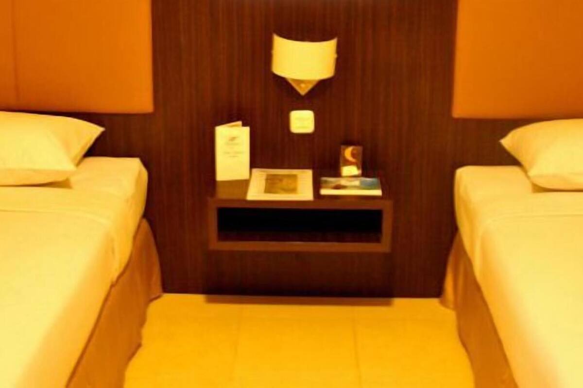 Habitación de hotel con dos camas, una mesita de noche, una lámpara y una pequeña mesa con un libro y un bloc de notas.