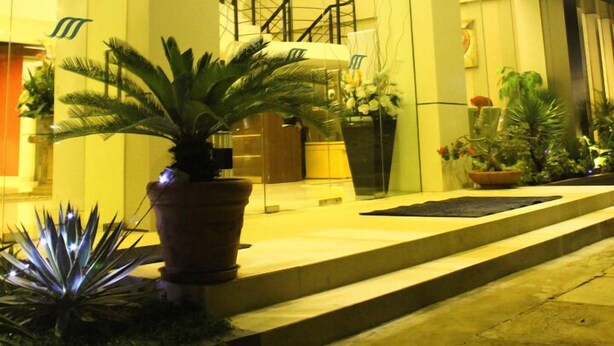 Une entrée d’hôtel moderne avec une façade en verre, un escalier et des plantes en pot.