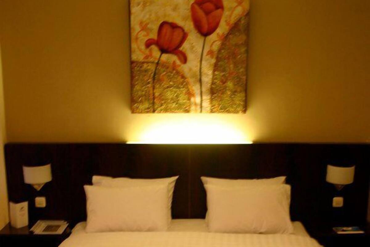Una habitación de hotel con una cama grande, dos mesitas de noche y un cuadro colgado en la pared con flores rojas.