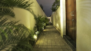 Un estrecho sendero adoquinado flanqueado por muros con plantas y una puerta de madera.