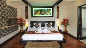Habitación de hotel con una cama grande, dos mesitas de noche, un televisor de pared y jarrones decorativos con flores.