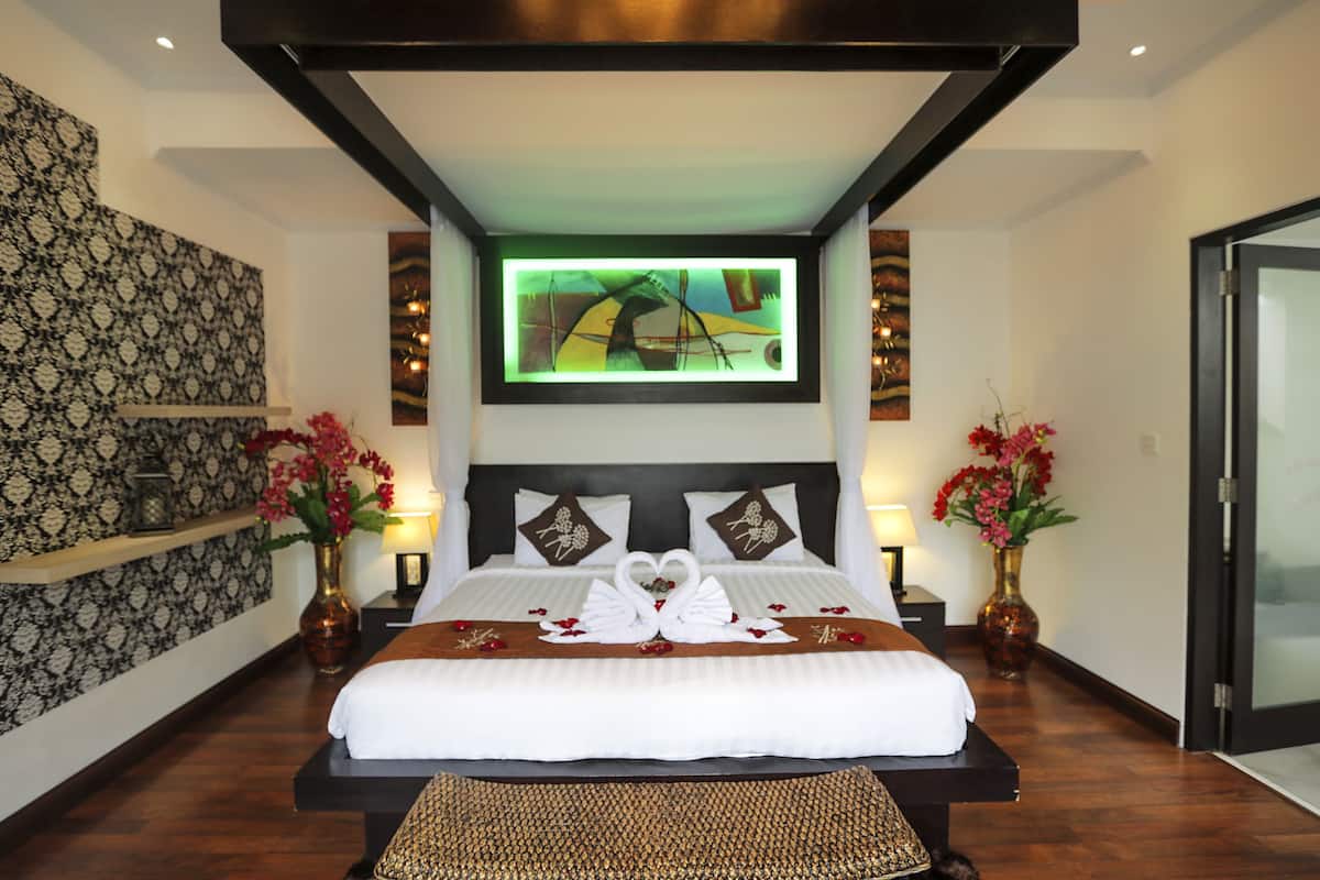 A hotel room with a large bed, two nightstands, a wall-mounted TV, and decorative vases with flowers.