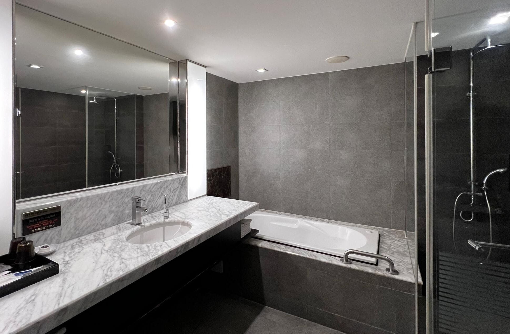 A modern bathroom with a large mirror, a dual sink vanity, a bathtub, and a glass-enclosed shower area.