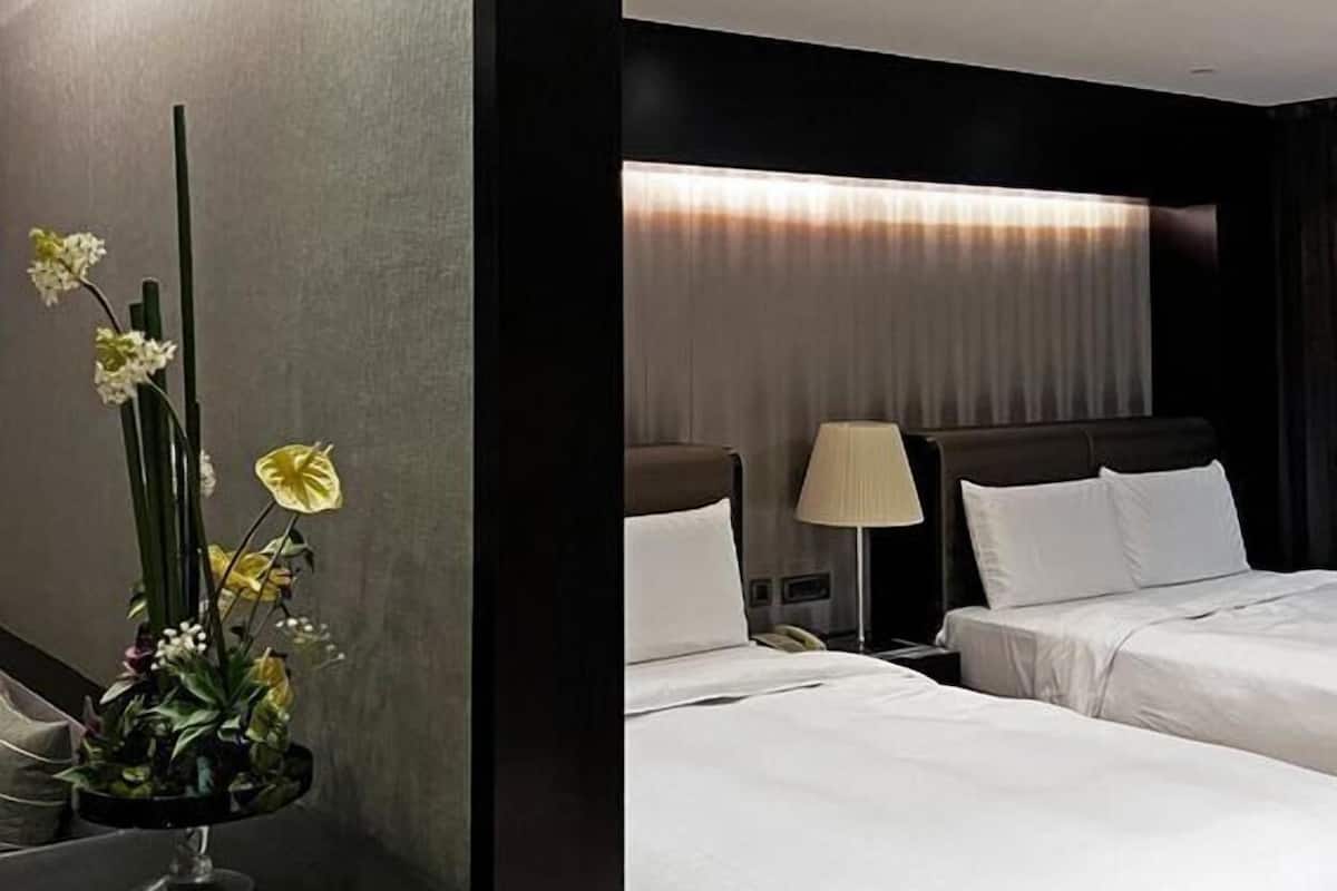 A hotel room with two beds, a bedside table, a lamp, and a mirror.