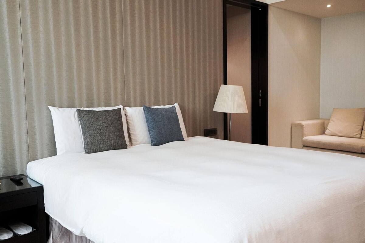 A hotel room with a large bed, a bedside table with a lamp, and a sofa.