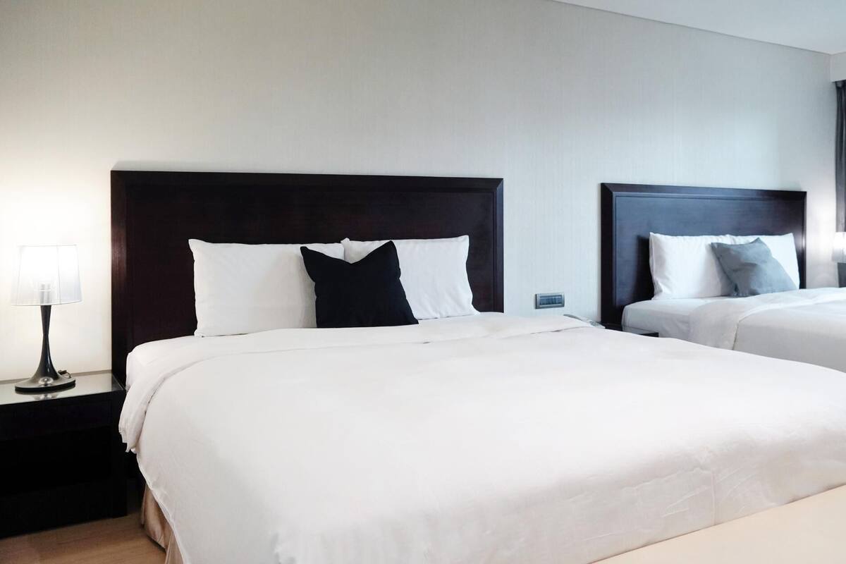 Two beds with dark headboards, white bedding, and a nightstand with a lamp.
