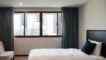A hotel room with a large window, a bed with white bedding, a chair, and a dark headboard.