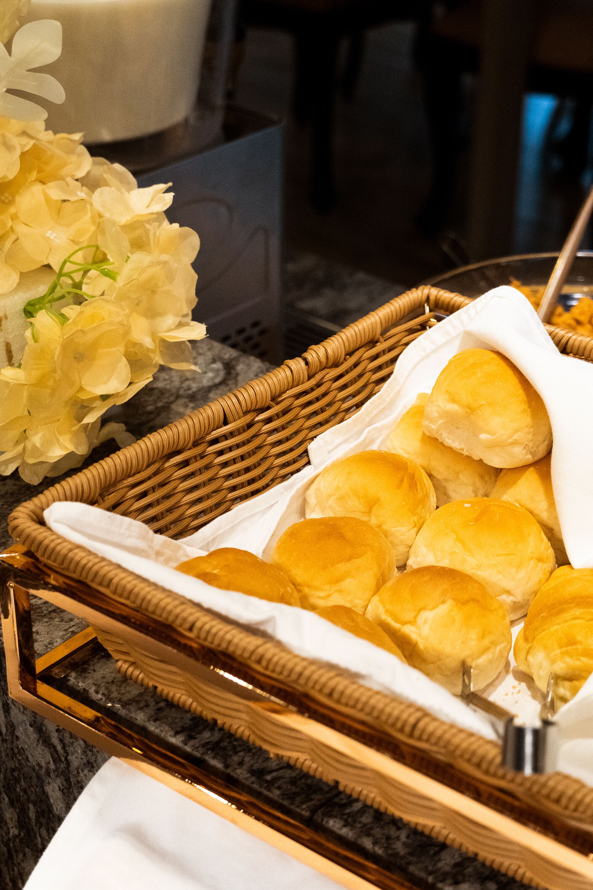 A wicker basket filled with rolls of bread, placed on a marble countertop.