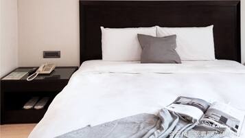 A neatly made bed with white and gray bedding, a bedside phone, and a magazine on the bed.