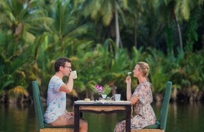 A couple sitting at a table by a water body, surrounded by lush greenery. - Canvas and Orchids Retreat (Koh Kong)
