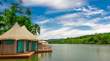 A floating tented accommodation with a view of a calm lake and lush greenery.