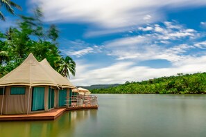 A floating tented accommodation with a view of a calm lake and lush greenery.