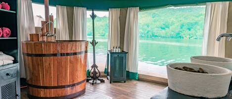 A cabin with a wooden barrel, a sink with a stone basin, and a view of a lake.