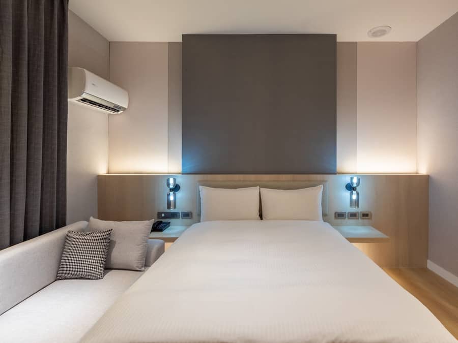 Quarto de hotel moderno com uma cama grande, um sofá, mesas de cabeceira e um aparelho de ar condicionado.