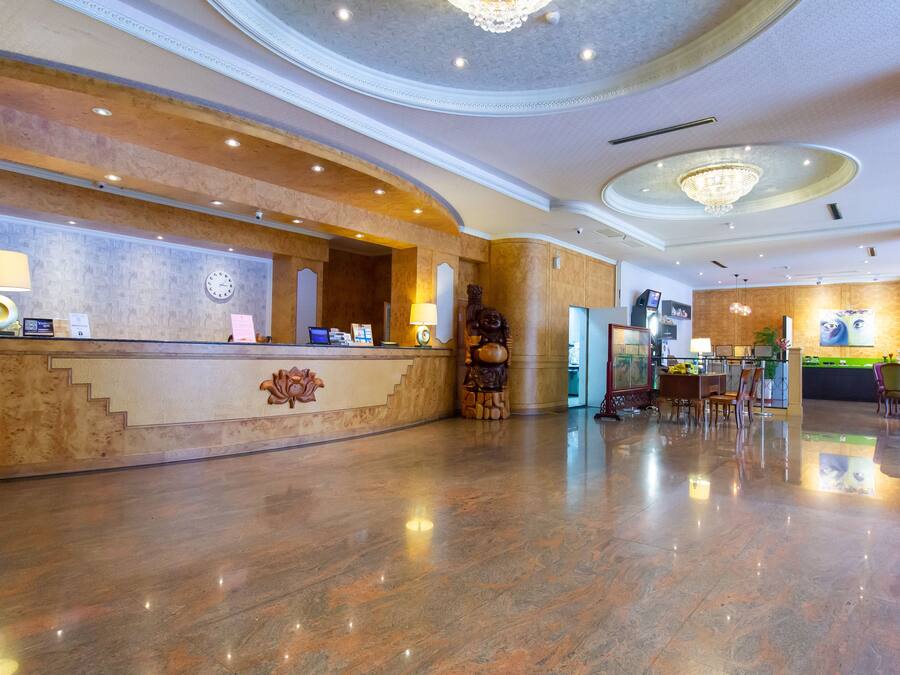 Un hall d’hôtel avec un sol en marbre, un comptoir d’accueil, une horloge et un lustre.