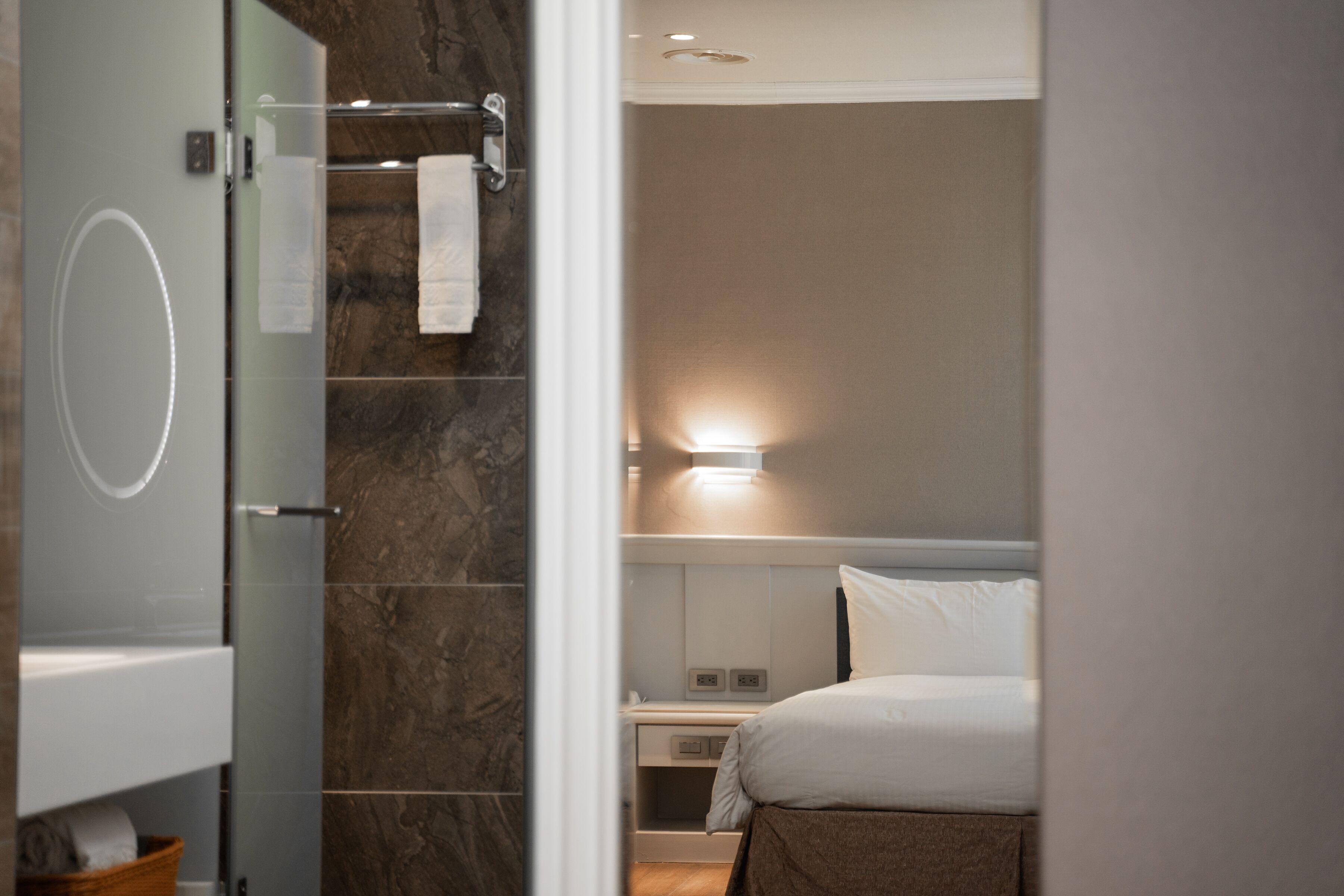 Un baño moderno con cabina de ducha de vidrio, pared de mármol y mesita de noche con lámpara.
