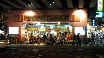 A busy street scene with a restaurant entrance, people walking, and scooters parked outside.