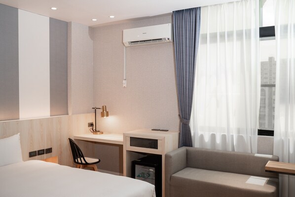 Une chambre d’hôtel comprenant un lit, un bureau, une chaise, un canapé, un climatiseur et une fenêtre avec des rideaux.