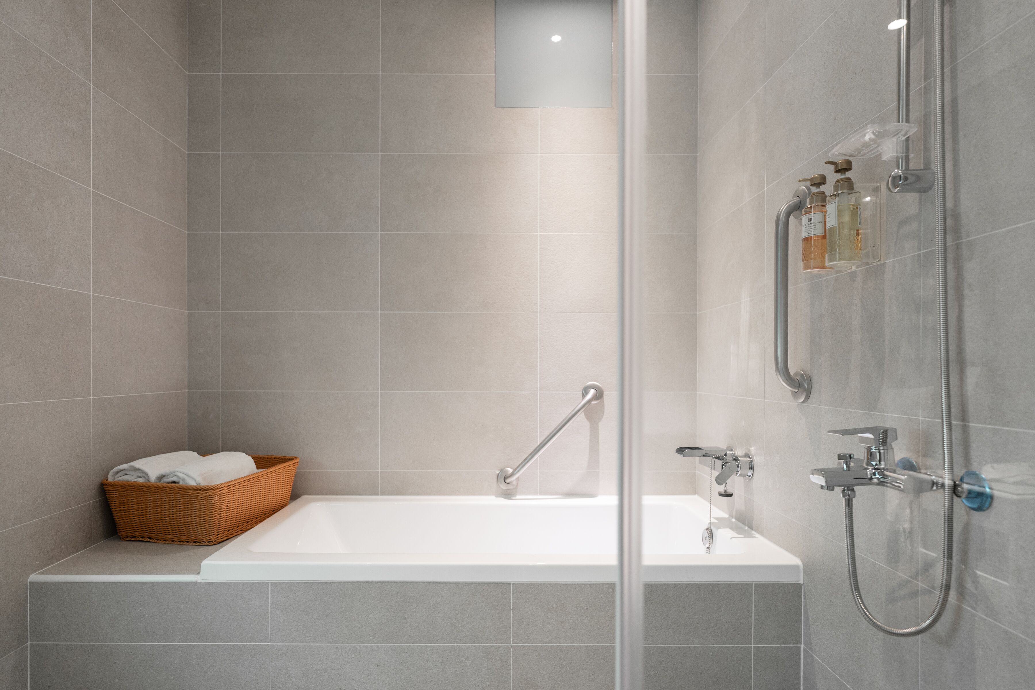 Ein modernes Badezimmer mit Badewanne, Dusche und einem Korbwäscher mit Handtüchern.