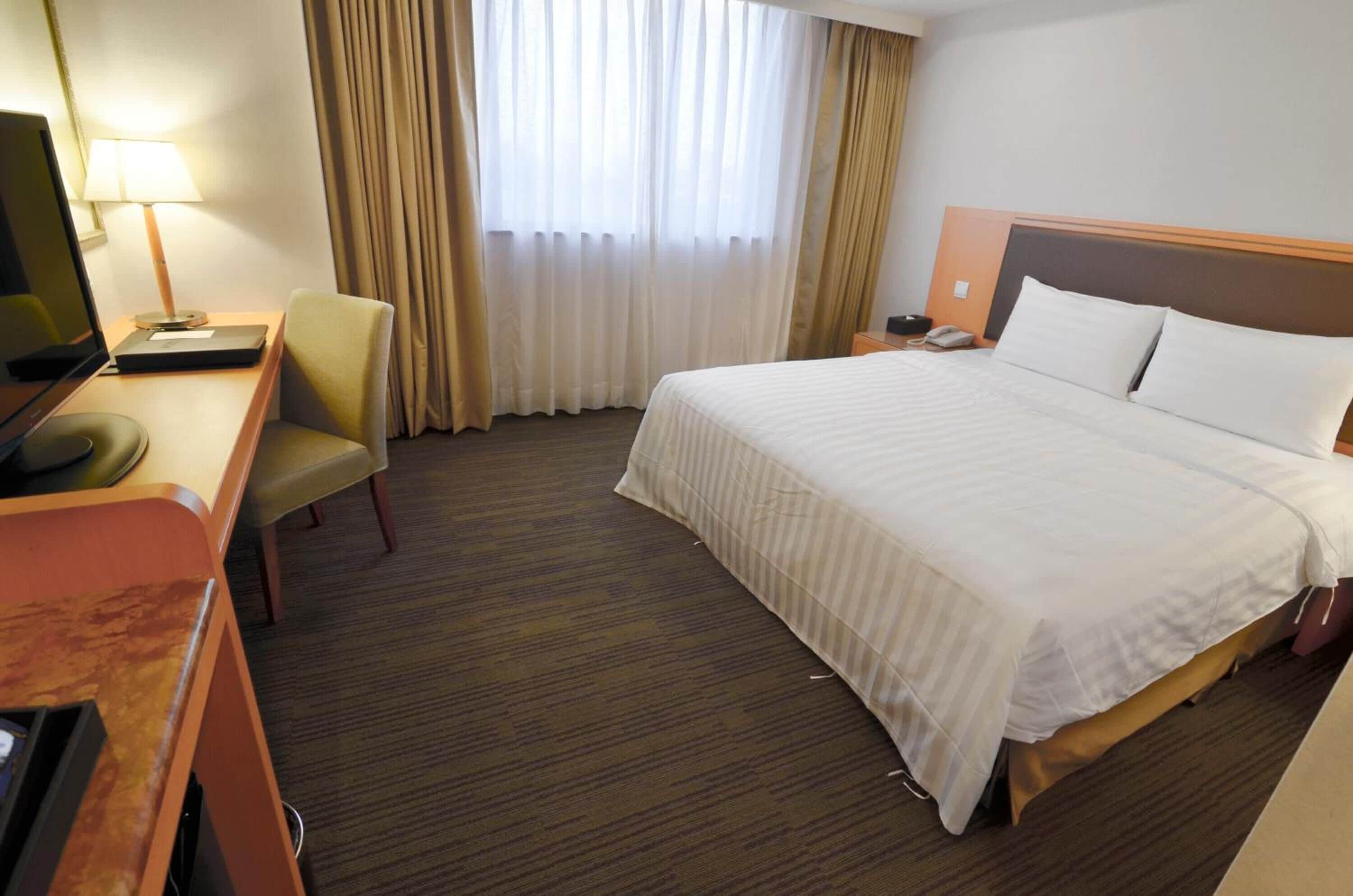Una camera d'albergo con un letto, una scrivania con un computer, una sedia e una televisione.