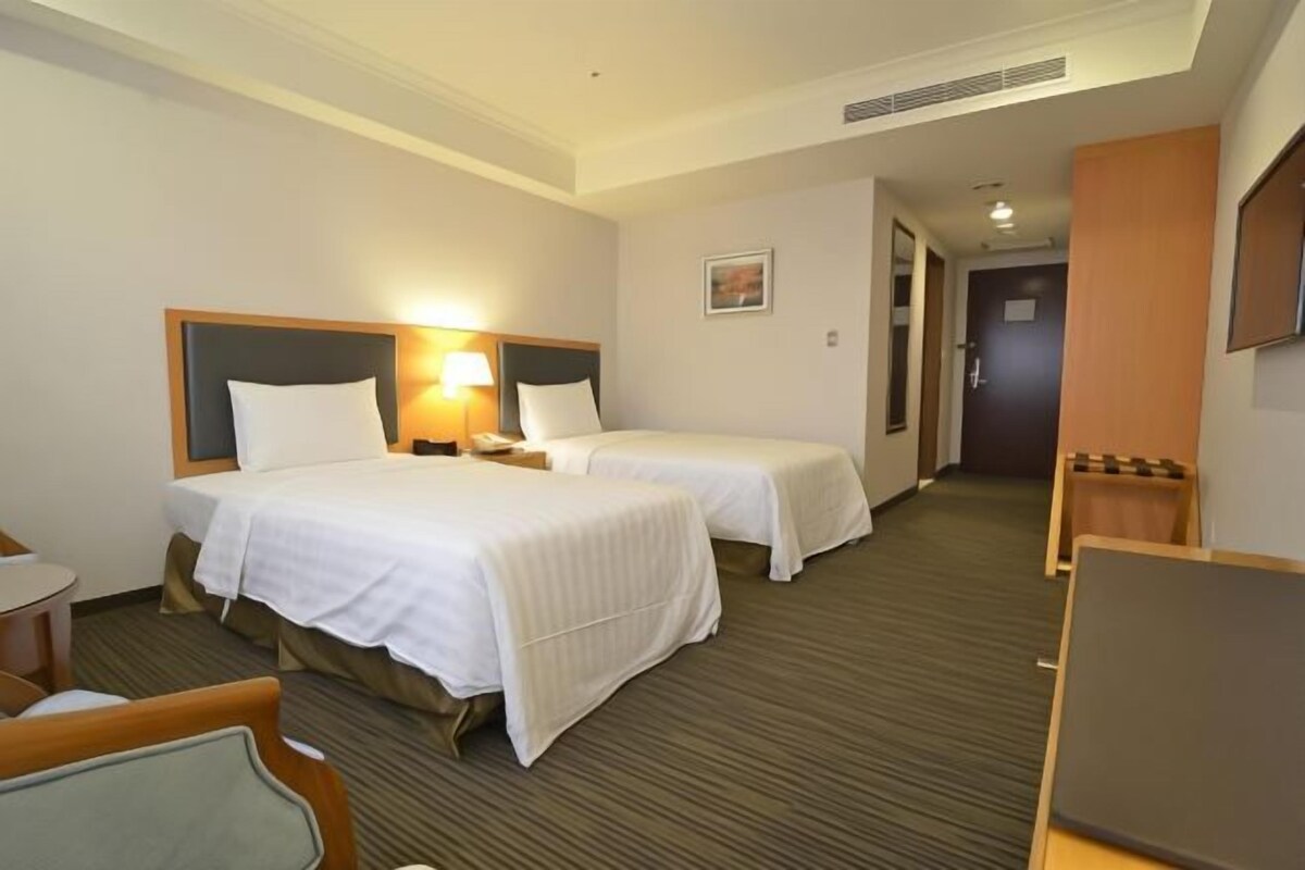 Una habitación de hotel con dos camas, un escritorio, una silla y una mesita.