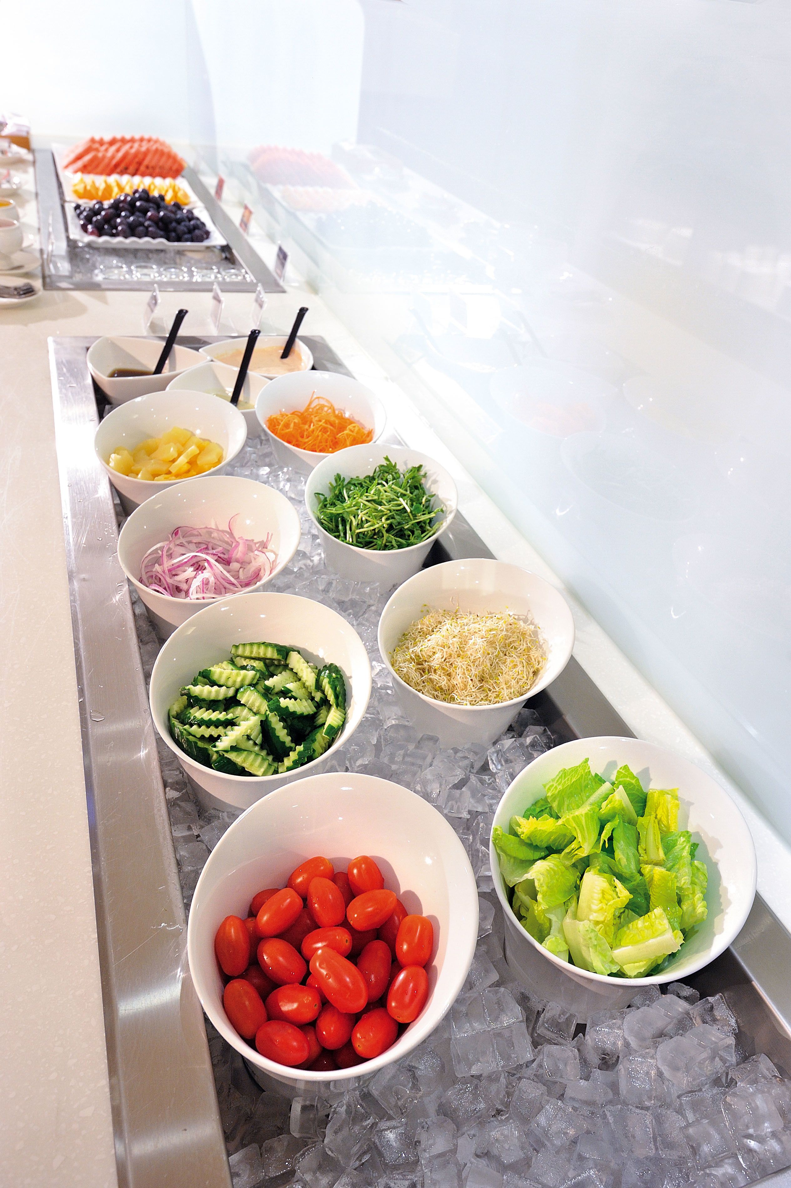 A buffet with various food items like vegetables, fruits, and cheeses arranged on a table with ice.