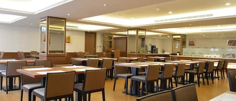 A spacious hotel dining area with multiple tables and chairs, a central bar area, and a large mirror reflecting the space.