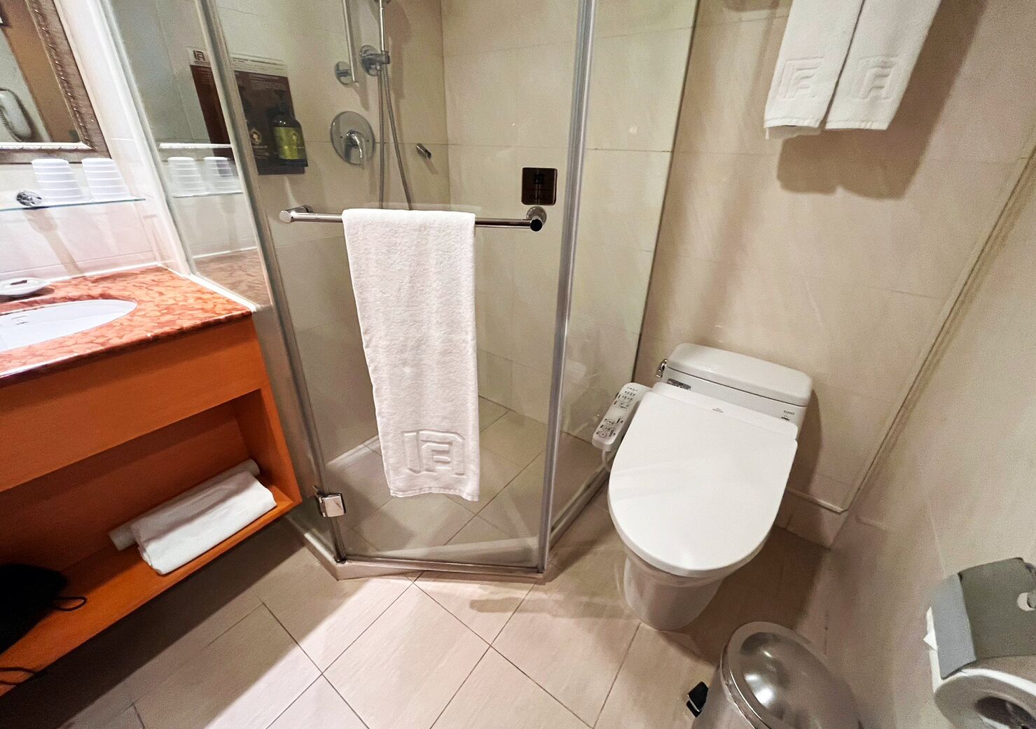 Un baño con cabina de ducha de vidrio, un inodoro blanco y un lavabo con toallero.