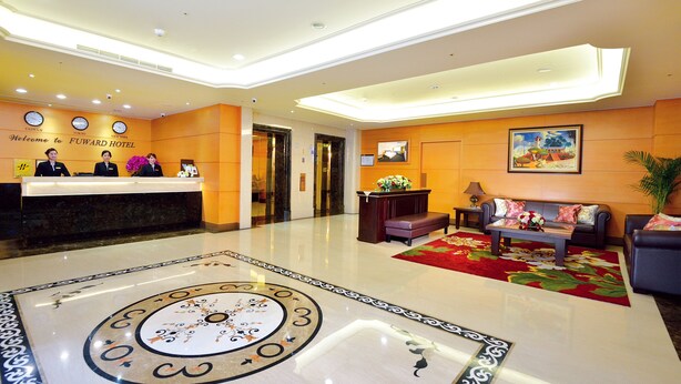 Un hall d’hôtel comprenant un comptoir d’accueil, trois employés, une horloge, un tableau, un canapé et une table basse.