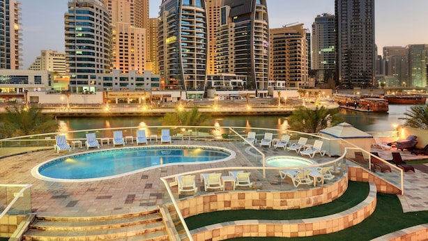 Un hotel moderno con una amplia piscina al aire libre, varios niveles de balcones y vistas al horizonte de la ciudad.