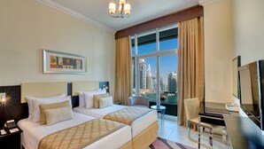 Habitación de hotel con dos camas, un escritorio, una silla, un televisor y un ventanal con vistas a la ciudad.
