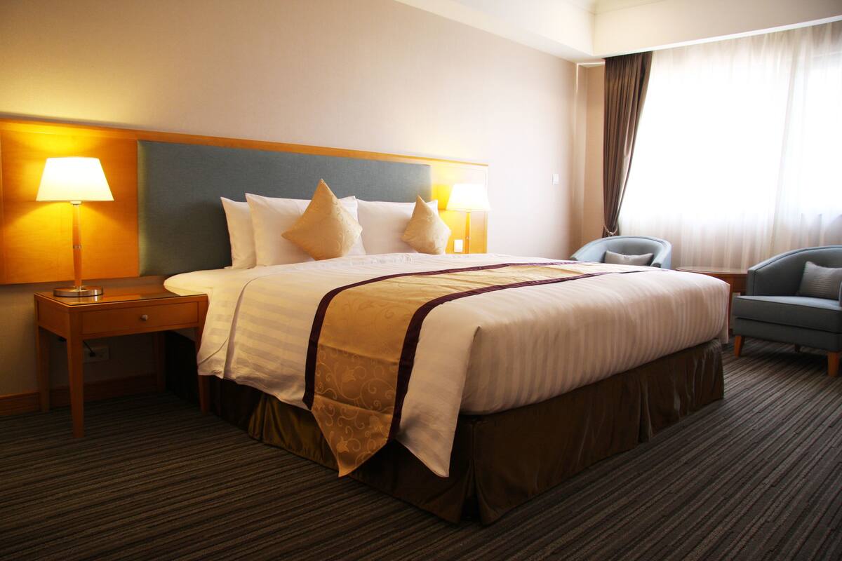 A hotel room with a large bed, two bedside lamps, a chair, and a window with curtains.