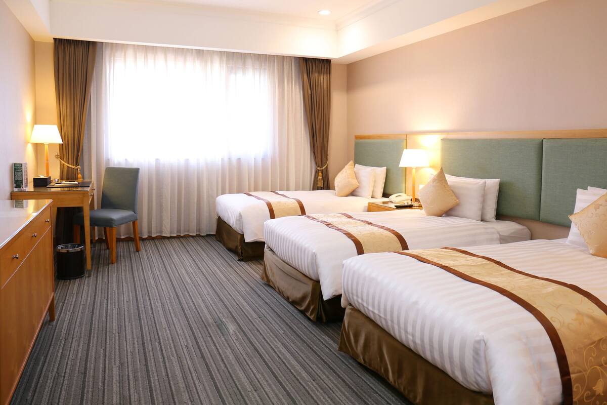 A hotel room with two beds, a desk, a chair, and a large window with curtains.