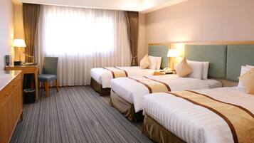 A hotel room with two beds, a desk, a chair, and a large window with curtains.
