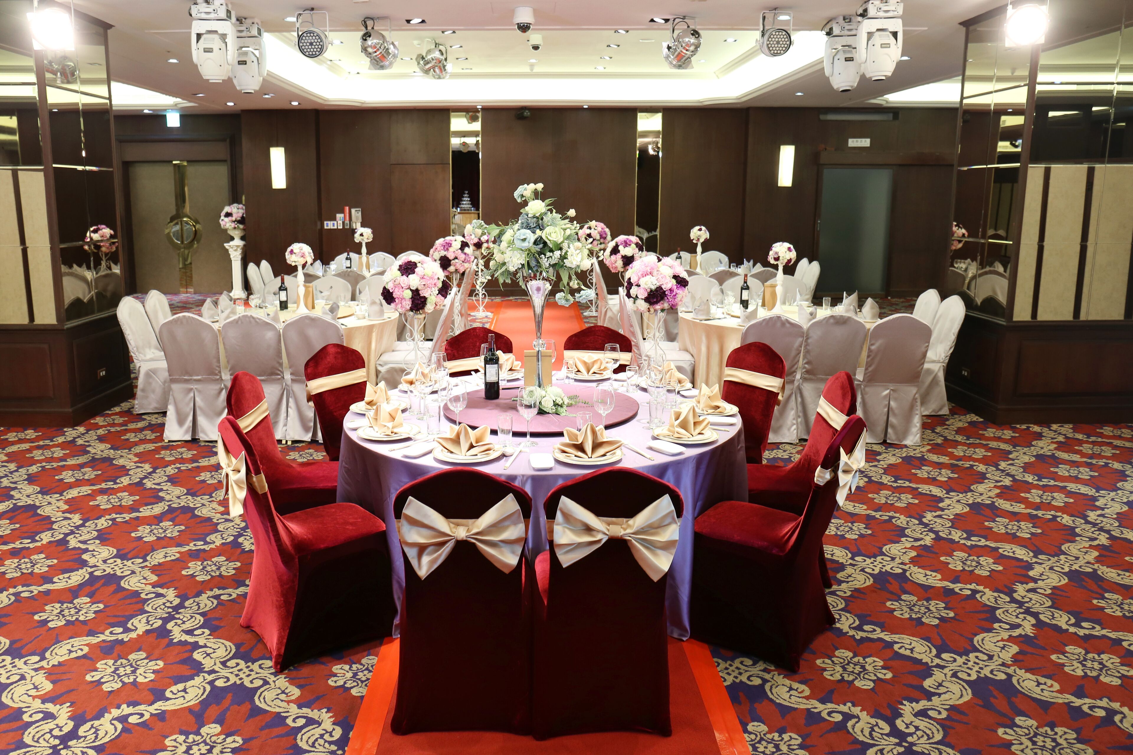 A banquet hall with round tables, red and white chairs, and floral centerpieces.
