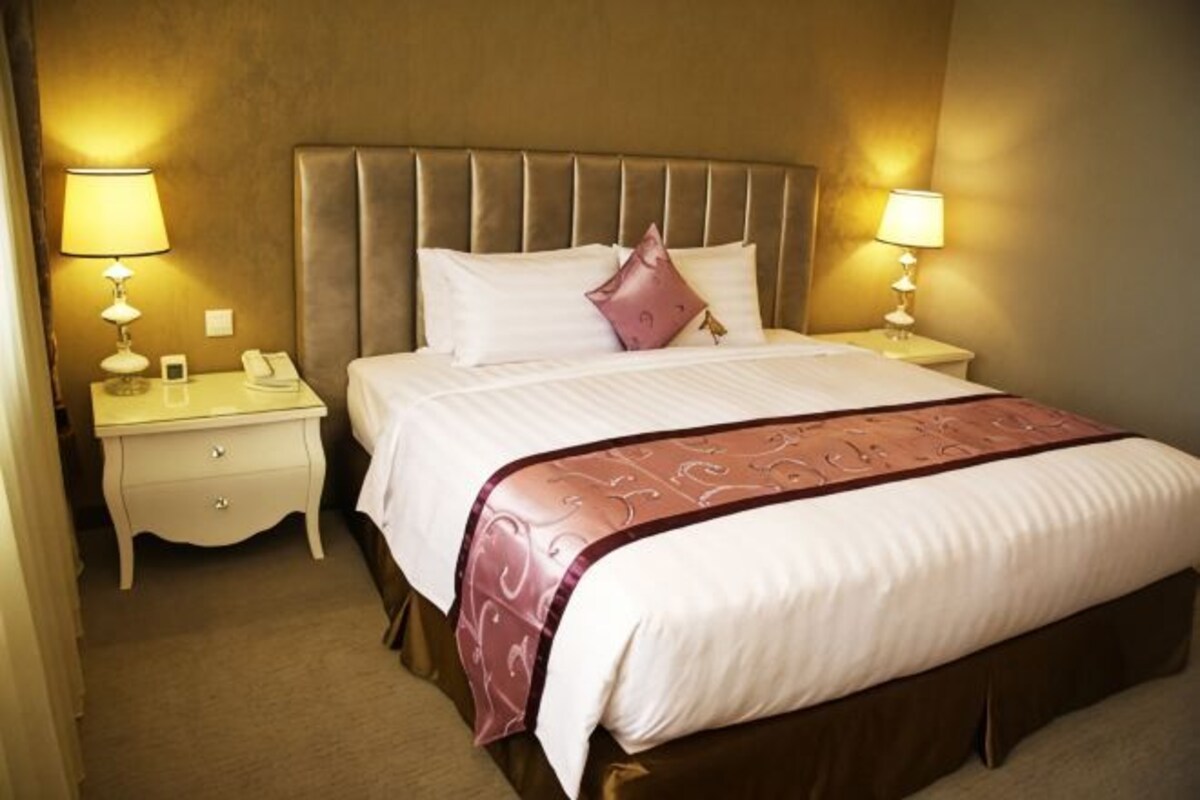 Quarto de hotel com uma cama grande, duas mesas de cabeceira e um criado-mudo.
