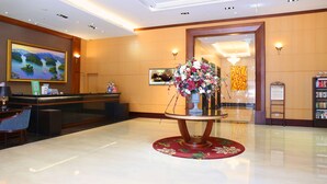 Un vestíbulo de hotel con mostrador de recepción, un gran arreglo floral, un cuadro en la pared y una estantería.