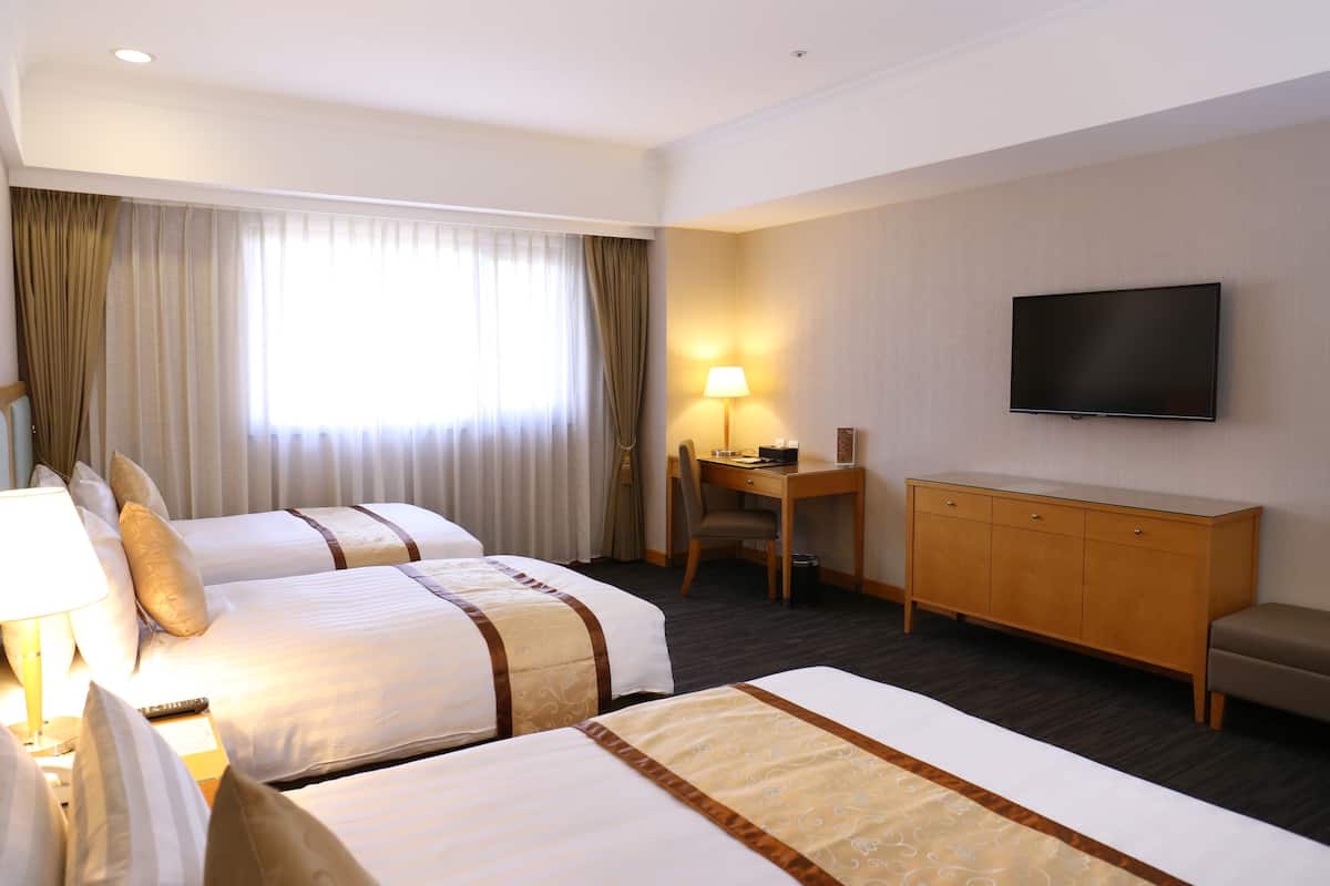 A hotel room with two beds, a desk, a chair, a television, and a window with curtains.
