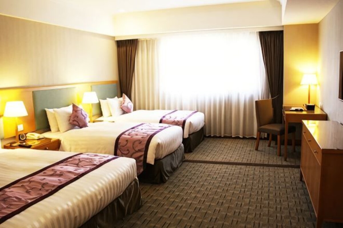 Quarto de hotel com três camas, uma escrivaninha e uma cadeira.