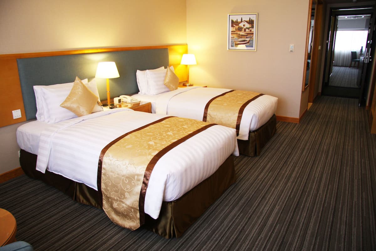 A hotel room with two beds, each with a headboard, bedside lamps, and a carpeted floor.