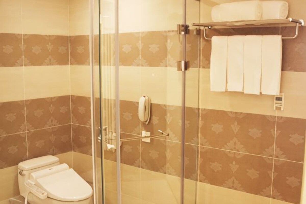 Casa de banho com cabine de chuveiro em vidro, sanita e um porta-toalhas com toalhas.