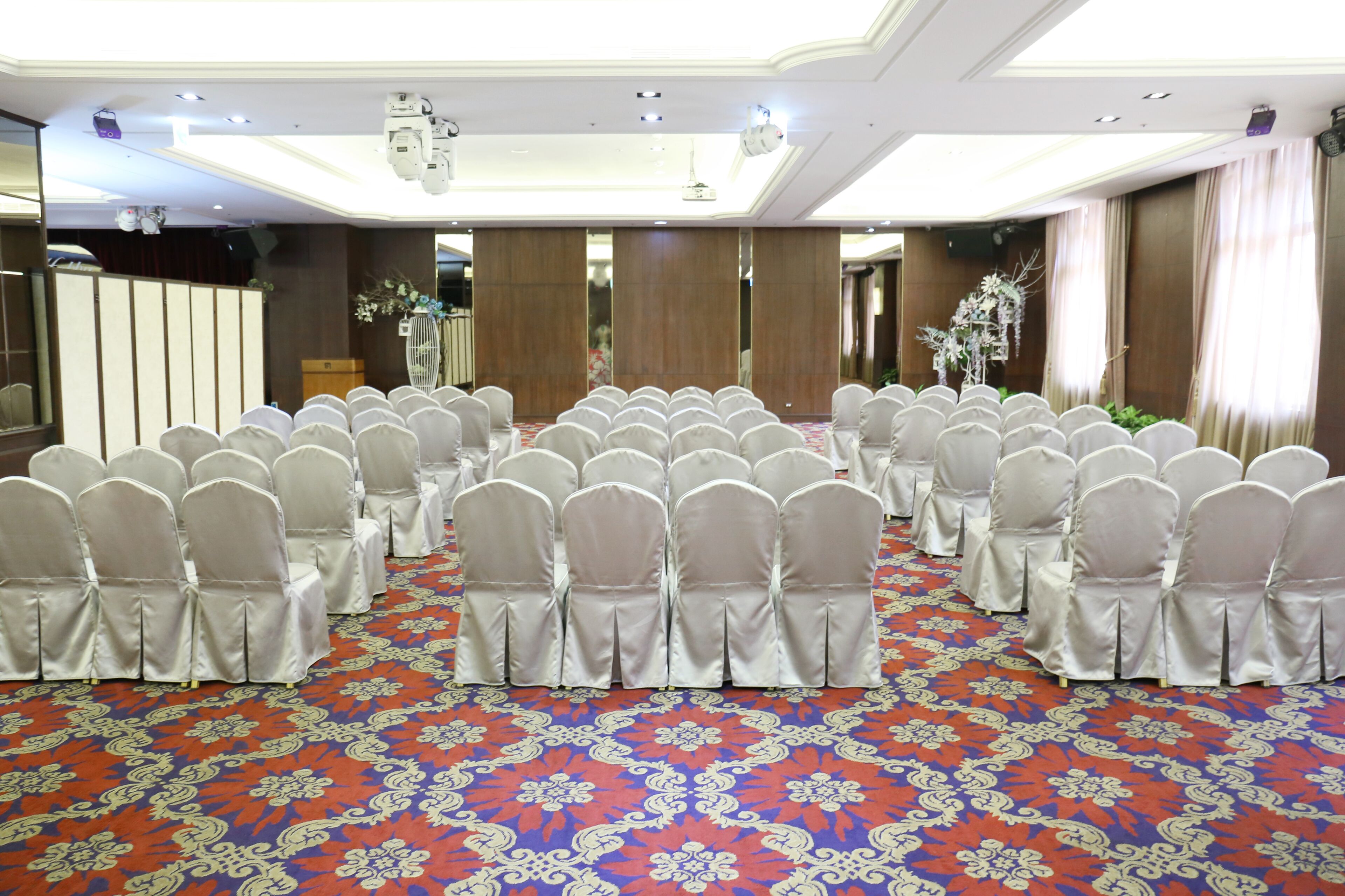 Un salón de conferencias con filas de sillas blancas y una alfombra estampada.