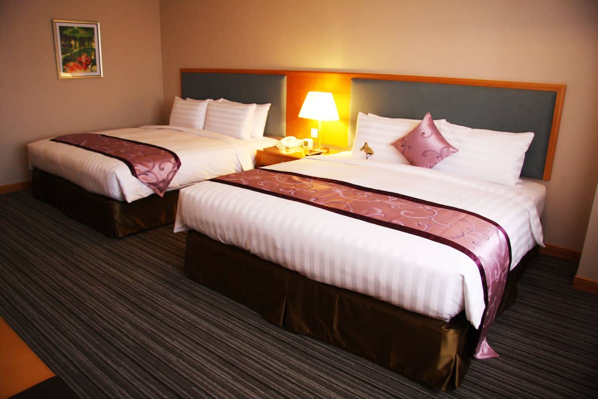 A hotel room with two beds, each with a headboard, a bedside table with a lamp, and a telephone.
