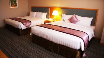 A hotel room with two beds, each with a headboard, a bedside table with a lamp, and a telephone.