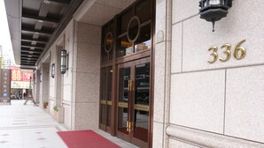 Entrada de un hotel con alfombra roja, amplias puertas de cristal y el número 336 en la pared.