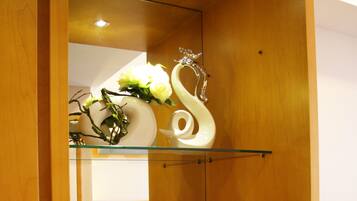 A hotel room with a wooden wardrobe, a mirror, a glass shelf with decorative items, a coffee maker, and bottled water.