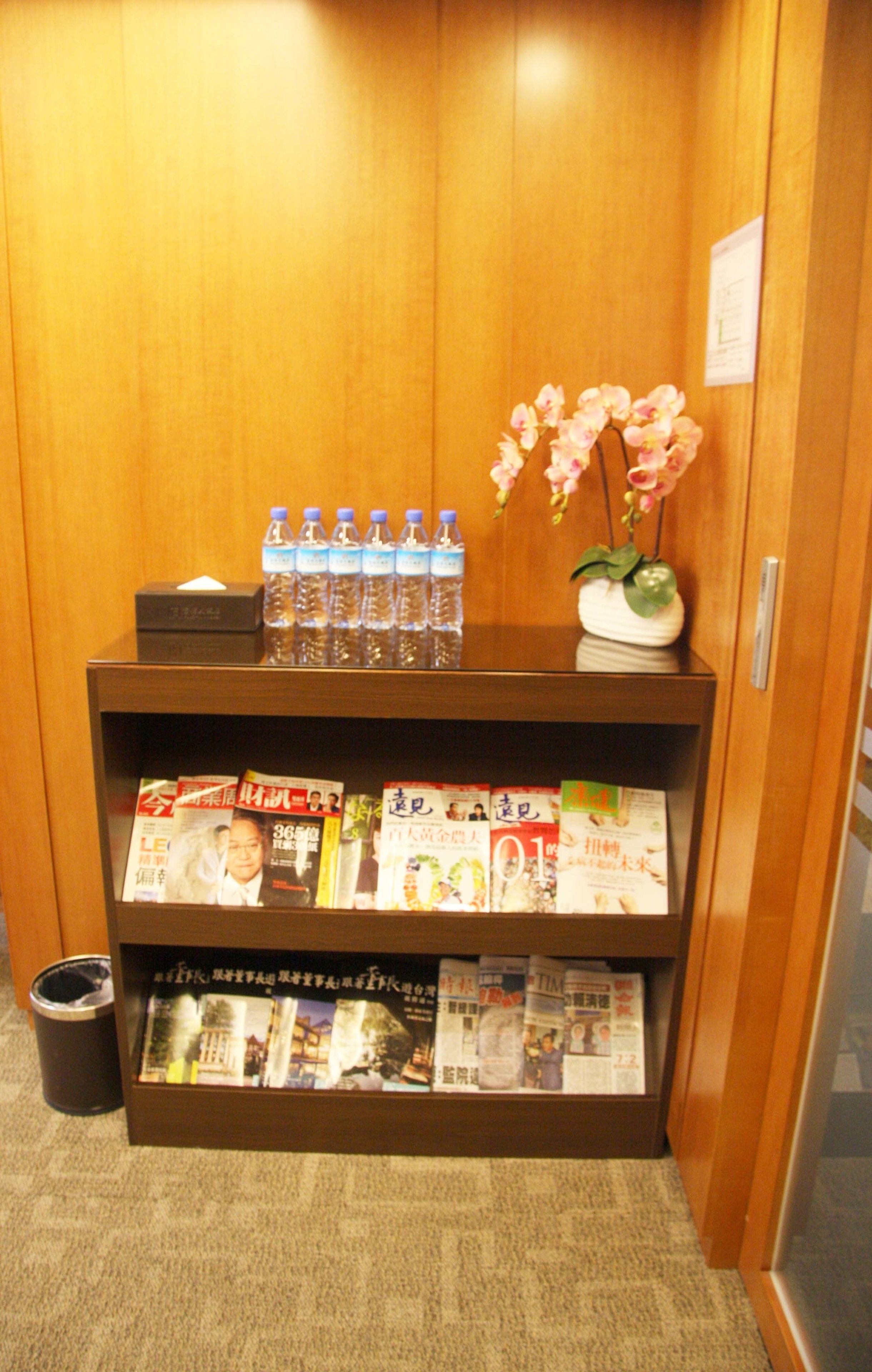 Un comptoir d’accueil en bois, avec des bouteilles d’eau, un vase rempli de fleurs roses et des magazines.