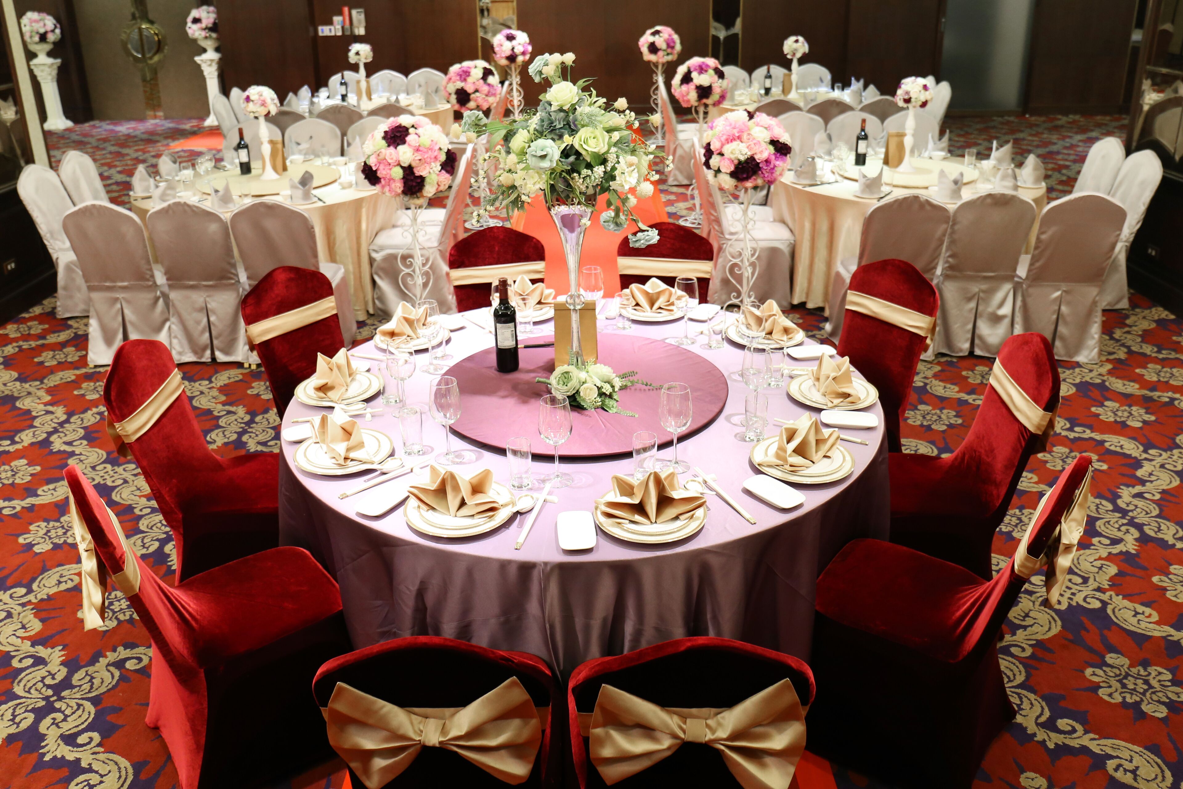 A round table with a purple tablecloth, surrounded by red chairs with gold sashes, set for a formal event.